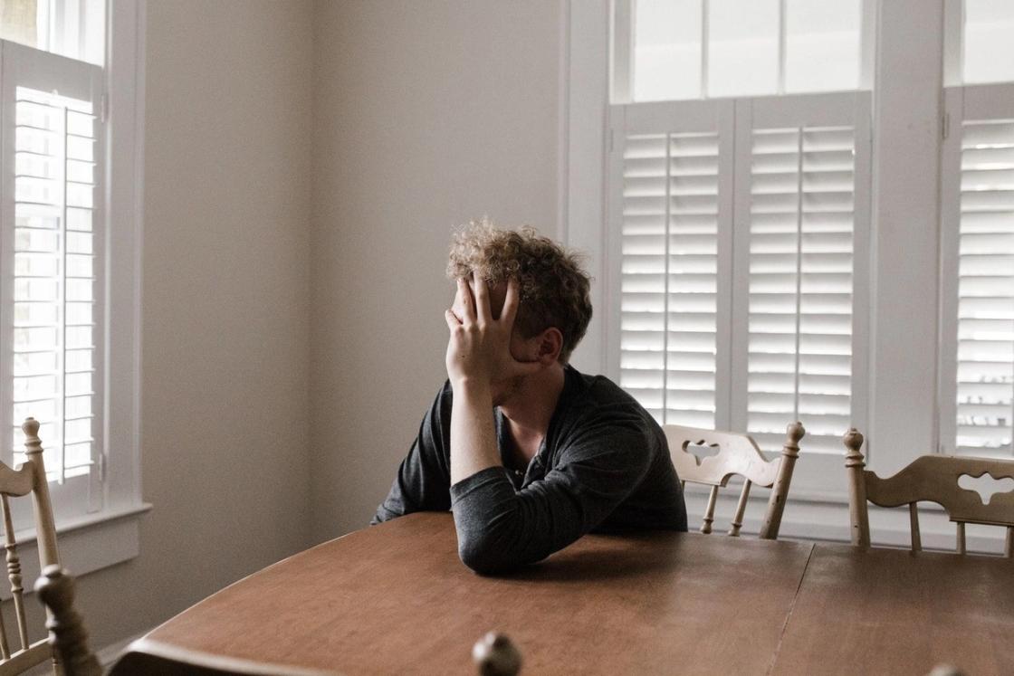 Person sitting alone at a dining table with head in hand, appearing overwhelmed and withdrawn, representing emotional distress associated with treatment-resistant depression.