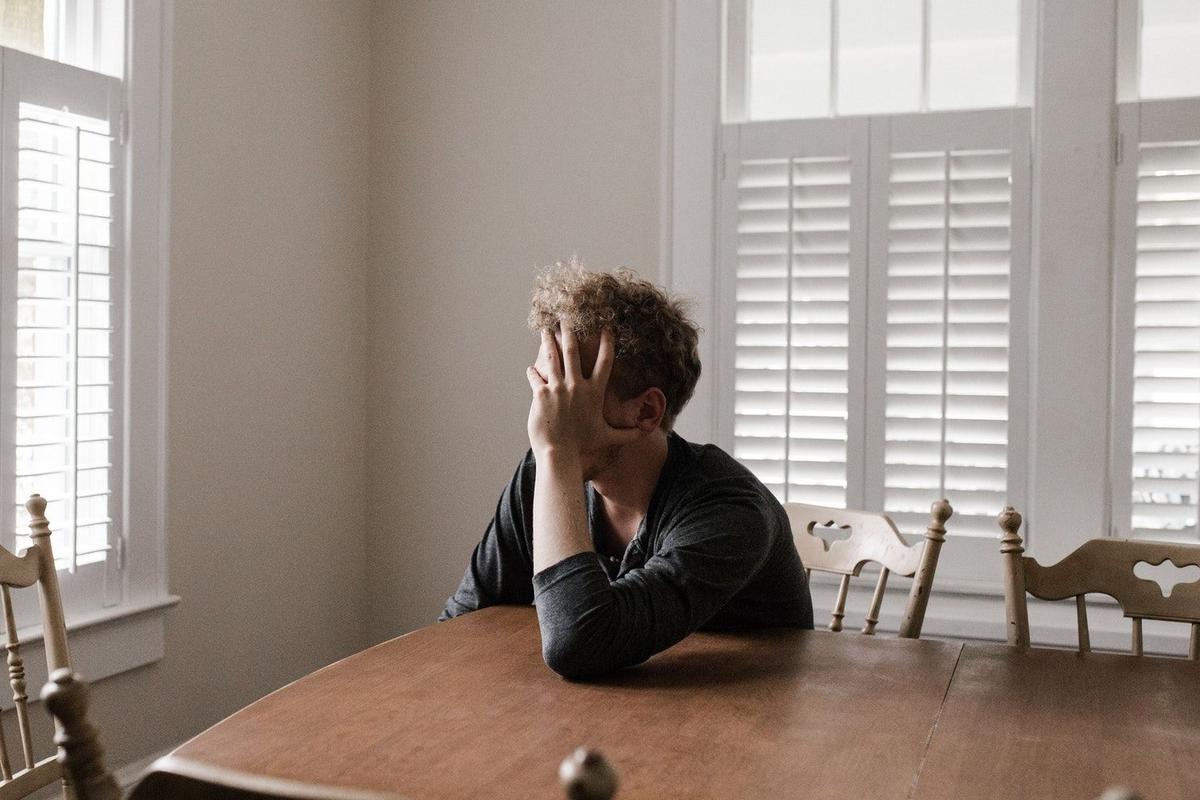 Person sitting alone at a dining table with head in hand, appearing overwhelmed and withdrawn, representing emotional distress associated with treatment-resistant depression.