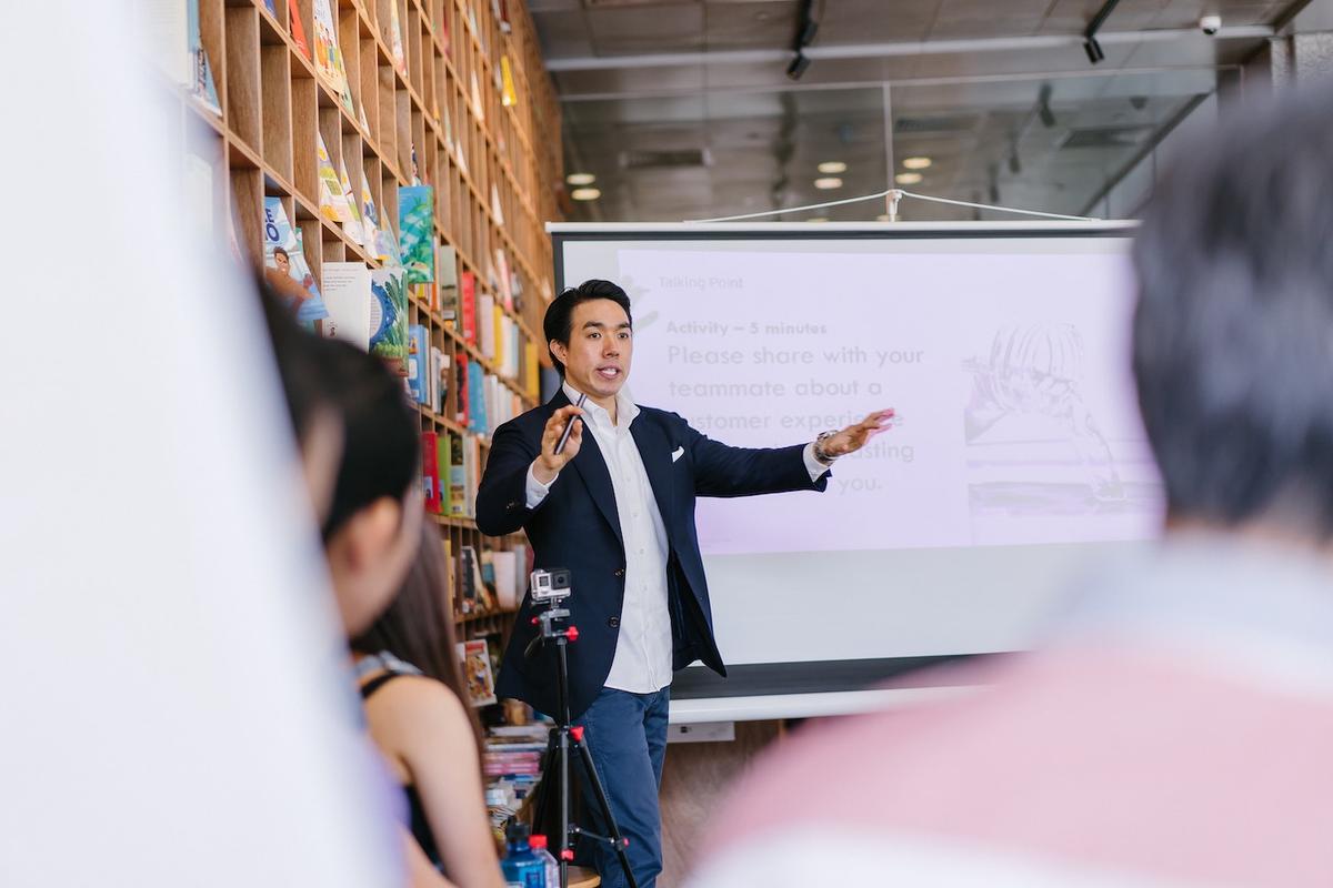 Man in business suit presenting to audience in contemporary office space with bookshelf backdrop, depicting professional success and executive pressure