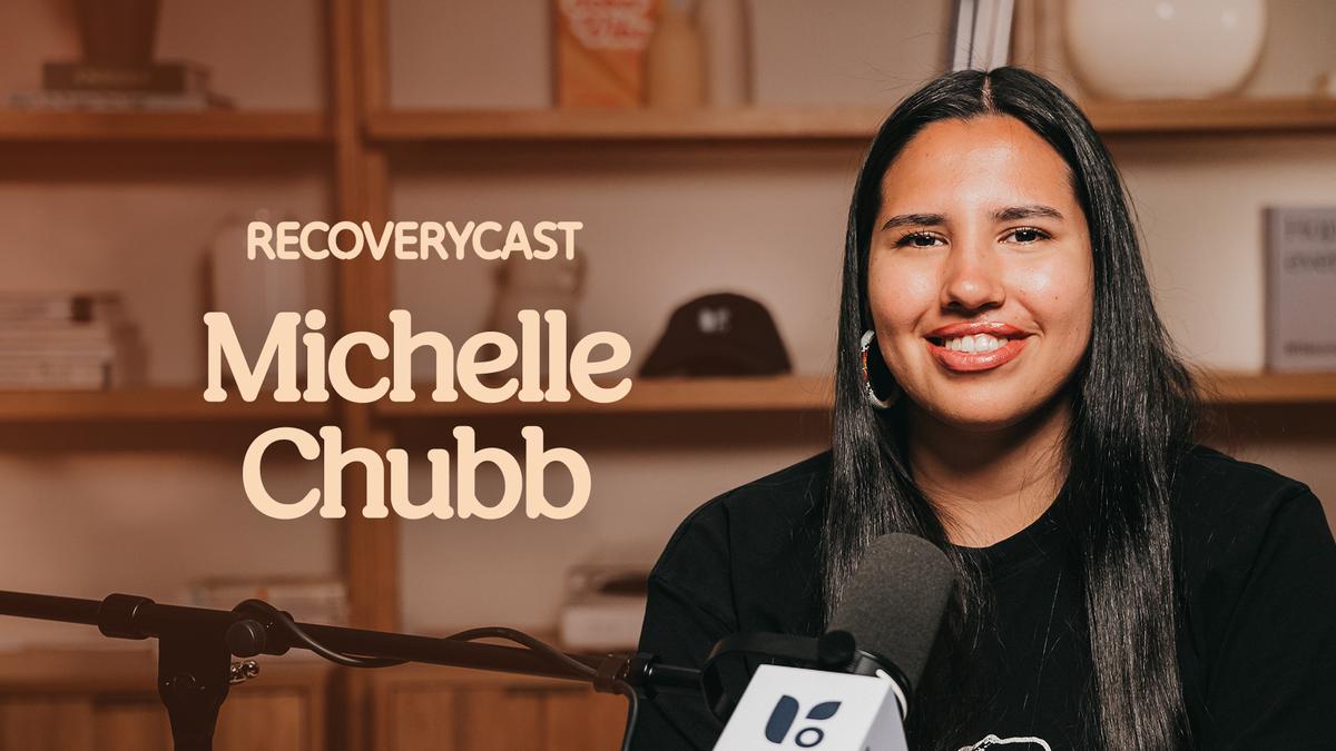 Michelle Chubb smiles while recording an episode of Recoverycast, with a podcast microphone in front of her and her name displayed on screen.