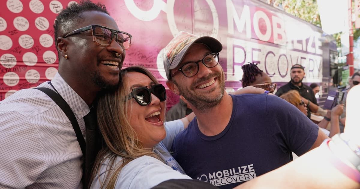 People smiling and taking a selfie at a Mobilize Recovery event celebrating community and addiction recovery support.