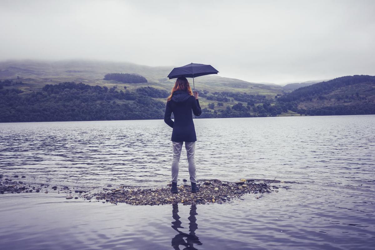 A woman with an umbrella standing on the shore of a lake.