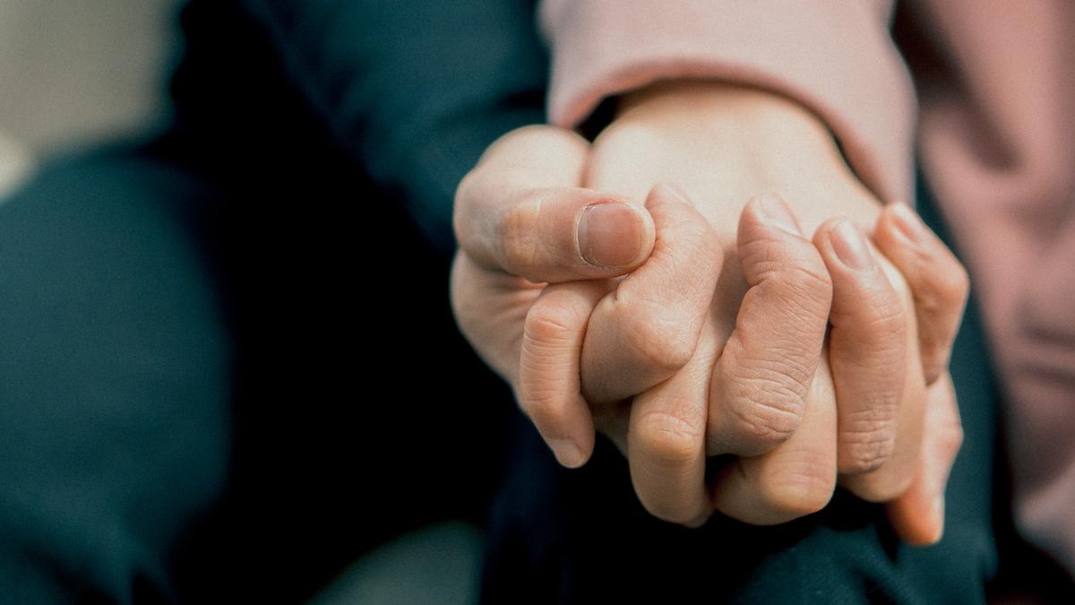Close-up of two people tightly interlocking their fingers and holding hands.