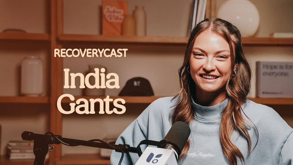 India Gans smiling during an interview on the Recoverycast podcast, with a microphone in front of her and her name displayed on screen.