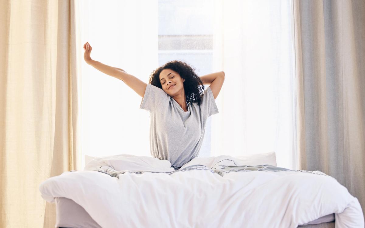 Woman waking up refreshed and stretching in bed with morning sunlight, representing improved sleep quality and energy from quitting alcohol