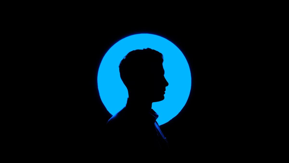 A side-profile silhouette of a person against a bright blue circular light on a black background.