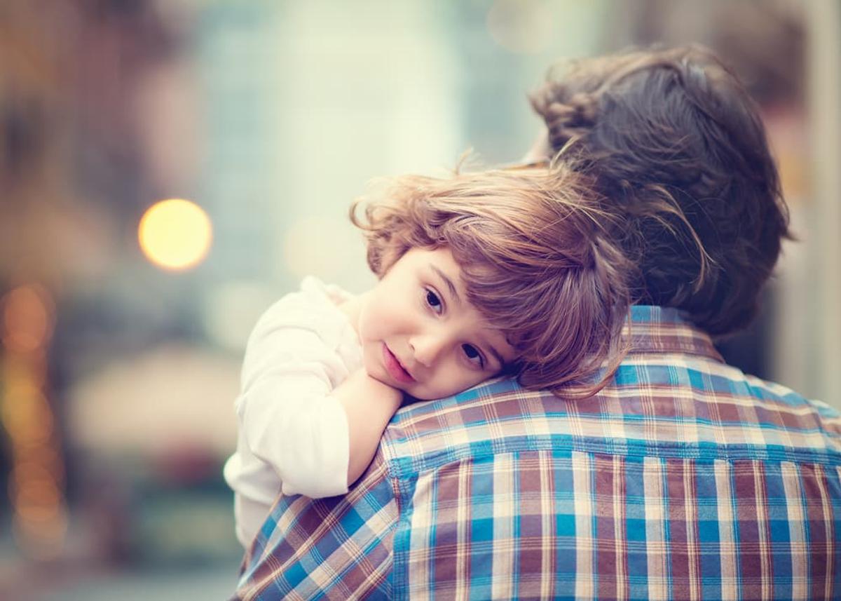 A young child rests their head on an adult’s shoulder in a quiet, outdoor setting, symbolizing family support, care, and the role loved ones can play in helping someone struggling with addiction.