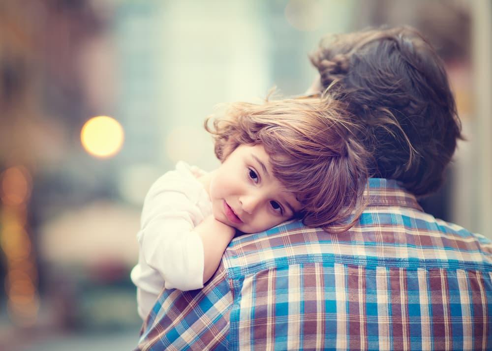 A young child rests their head on an adult’s shoulder in a quiet, outdoor setting, symbolizing family support, care, and the role loved ones can play in helping someone struggling with addiction.