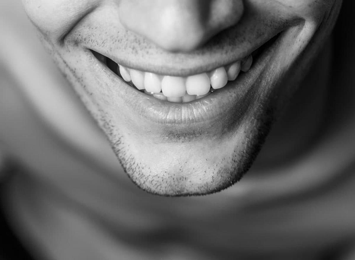 Black-and-white close-up of a smiling mouth, showing teeth and light facial stubble.