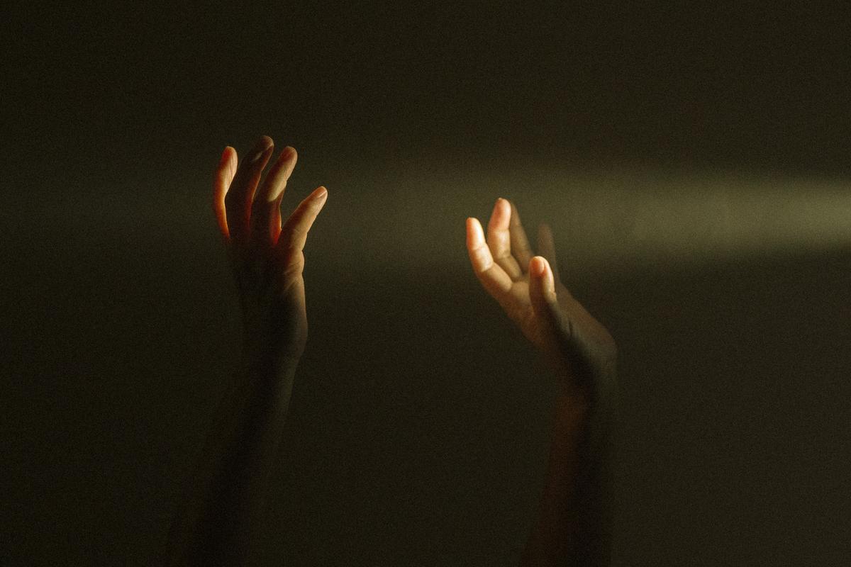 Two hands reaching upward into a soft beam of light against a dark, moody background.