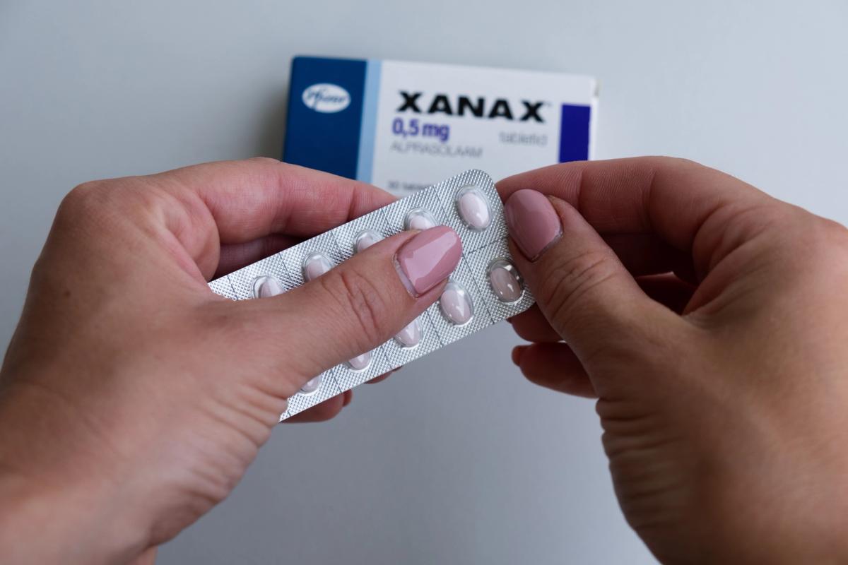 Hands holding a blister pack of Xanax (alprazolam) tablets with a Xanax 0.5 mg box in the background, illustrating prescription anti-anxiety medication use.