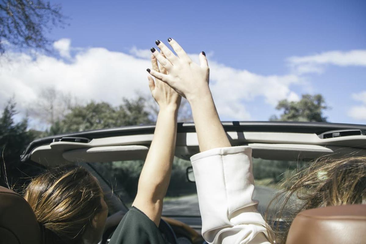 Two people in convertible car with hands raised, depicting carefree driving behavior and potential distracted driving risks