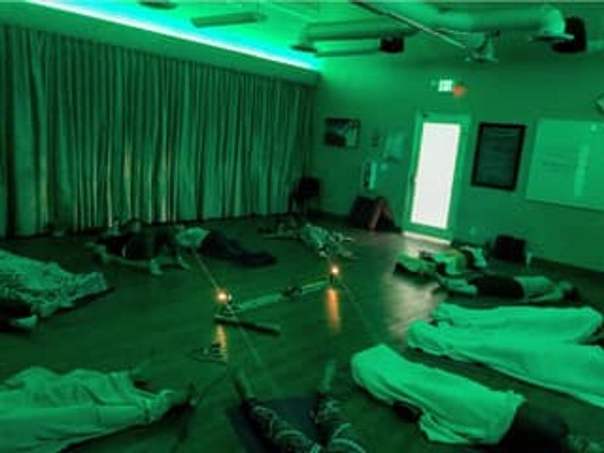 A group of people lying on yoga mats in a dimly lit room bathed in vibrant green light.