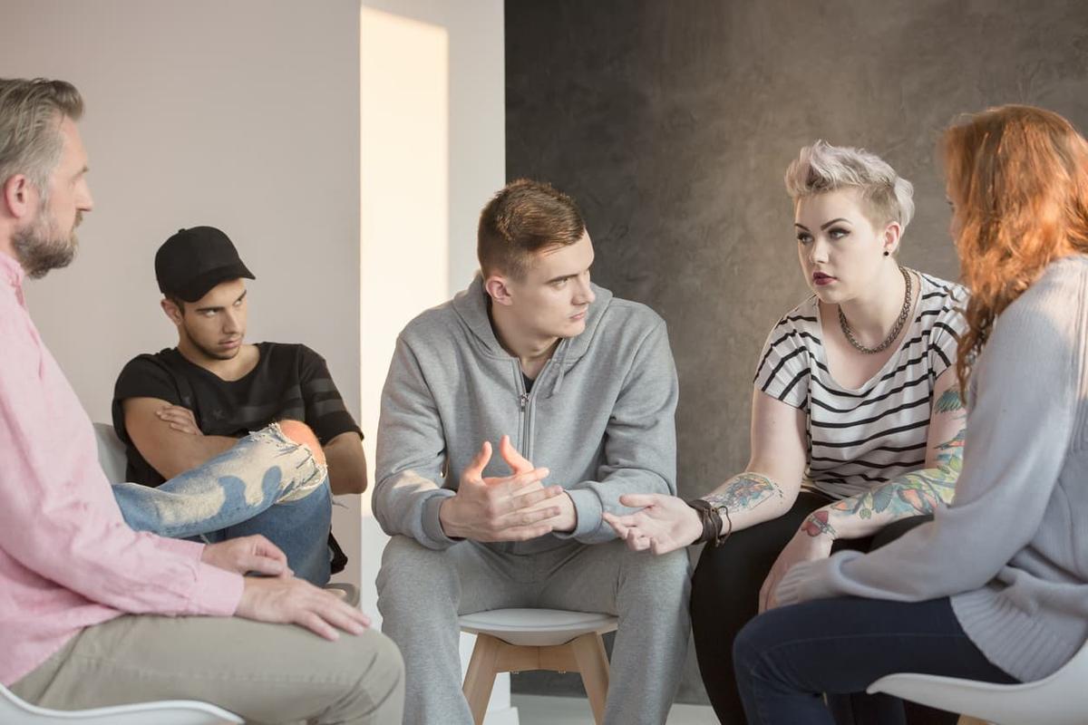 A small group of adults seated in a circle during an AA meeting, engaged in a serious discussion, illustrating peer support, counseling, and shared experiences in addiction treatment.