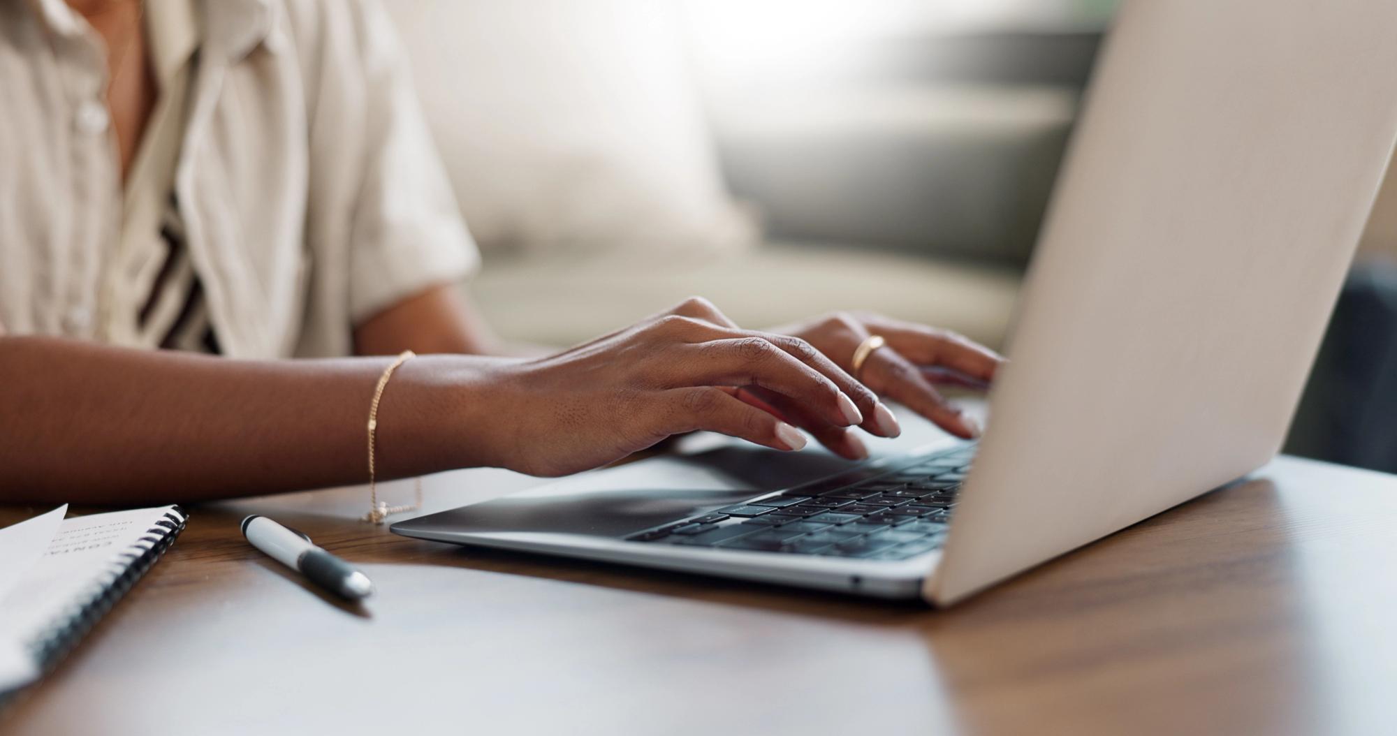 Person typing on a laptop while reviewing notes for an editorial policy document.
