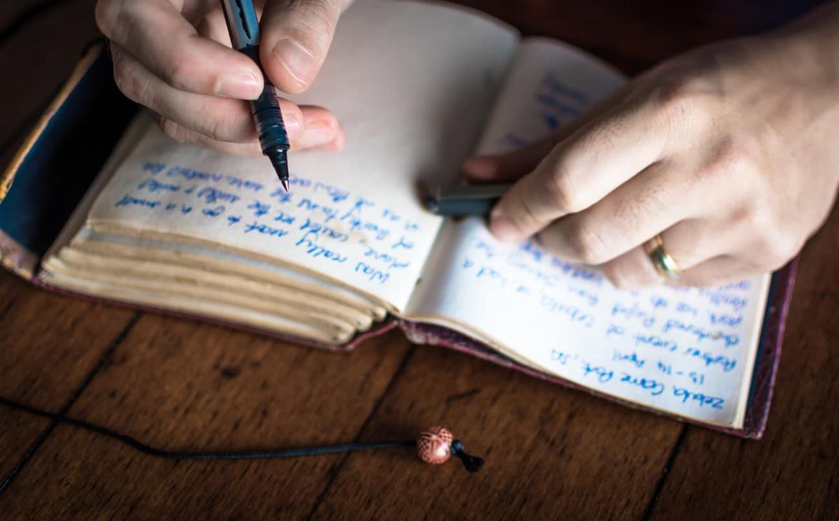 Close-up of hands writing in a journal with a pen, symbolizing recovery journaling, self-reflection, and coping strategies for addiction or mental health treatment.