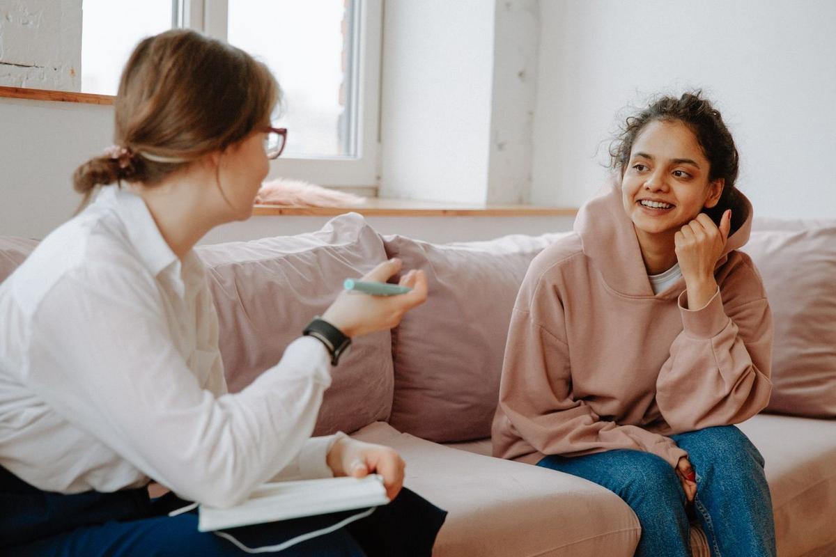 Mental health professional conducting trauma-informed counseling with smiling client on couch in warm, welcoming therapy space