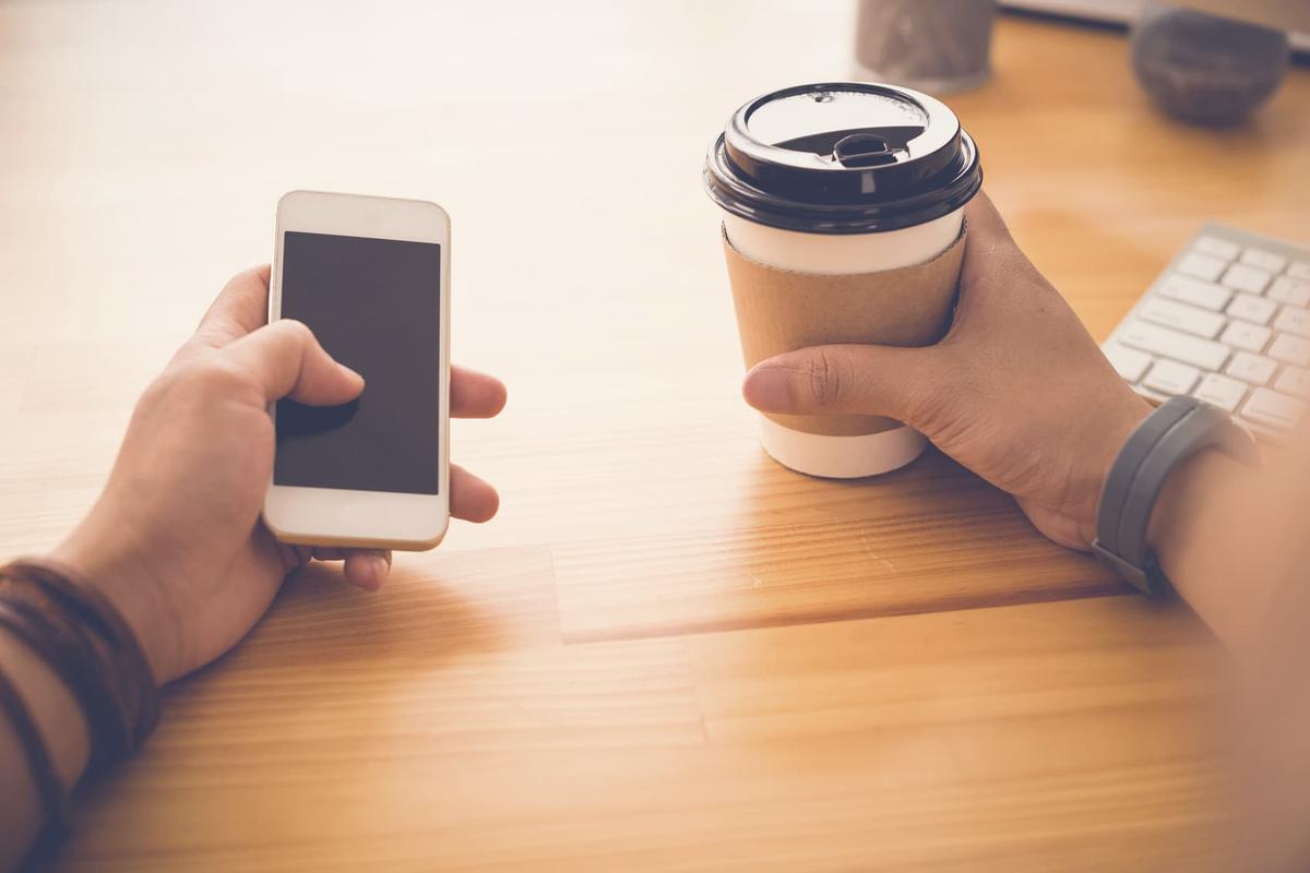 Person holding smartphone and coffee cup at desk, showing common substitute addictions like caffeine and technology in recovery