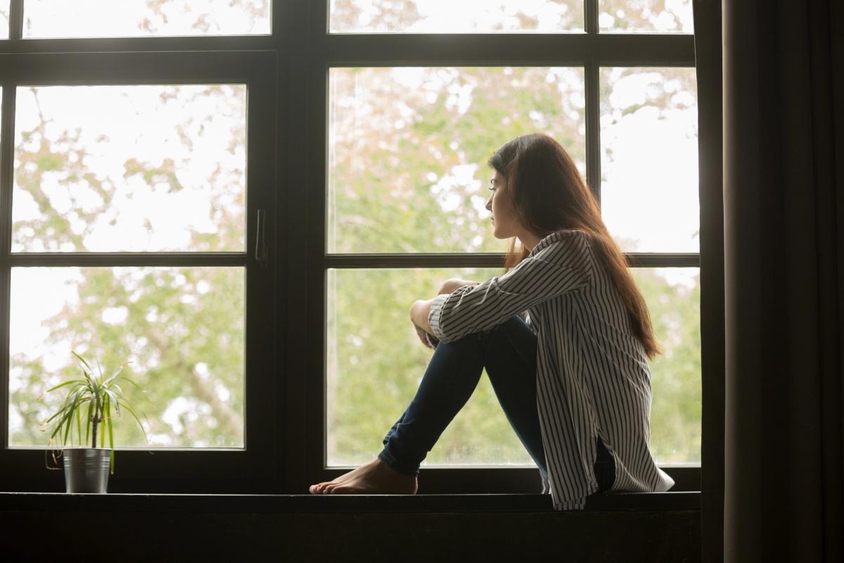 Woman sitting quietly by a window, reflecting in natural light, symbolizing introspection, emotional healing, and mental health recovery.