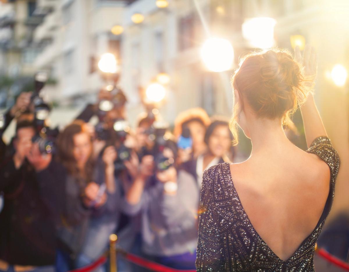 Celebrity in sparkly dress at media event with photographers and bright camera flashes, illustrating the pressures of fame and mental health challenges