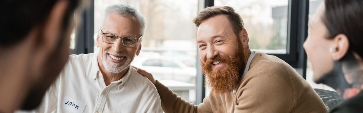 Two men smiling and talking during a relapse prevention support group, with others seated nearby in a bright, welcoming meeting space.