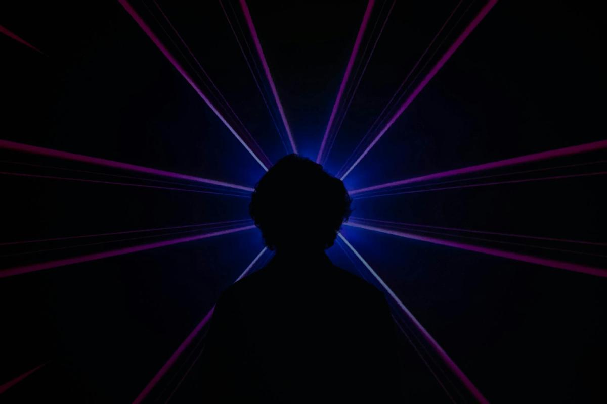 Silhouetted person facing outward as purple and blue light rays radiate from their head against a dark background, illustrating altered perception and the question “is LSD addictive.”