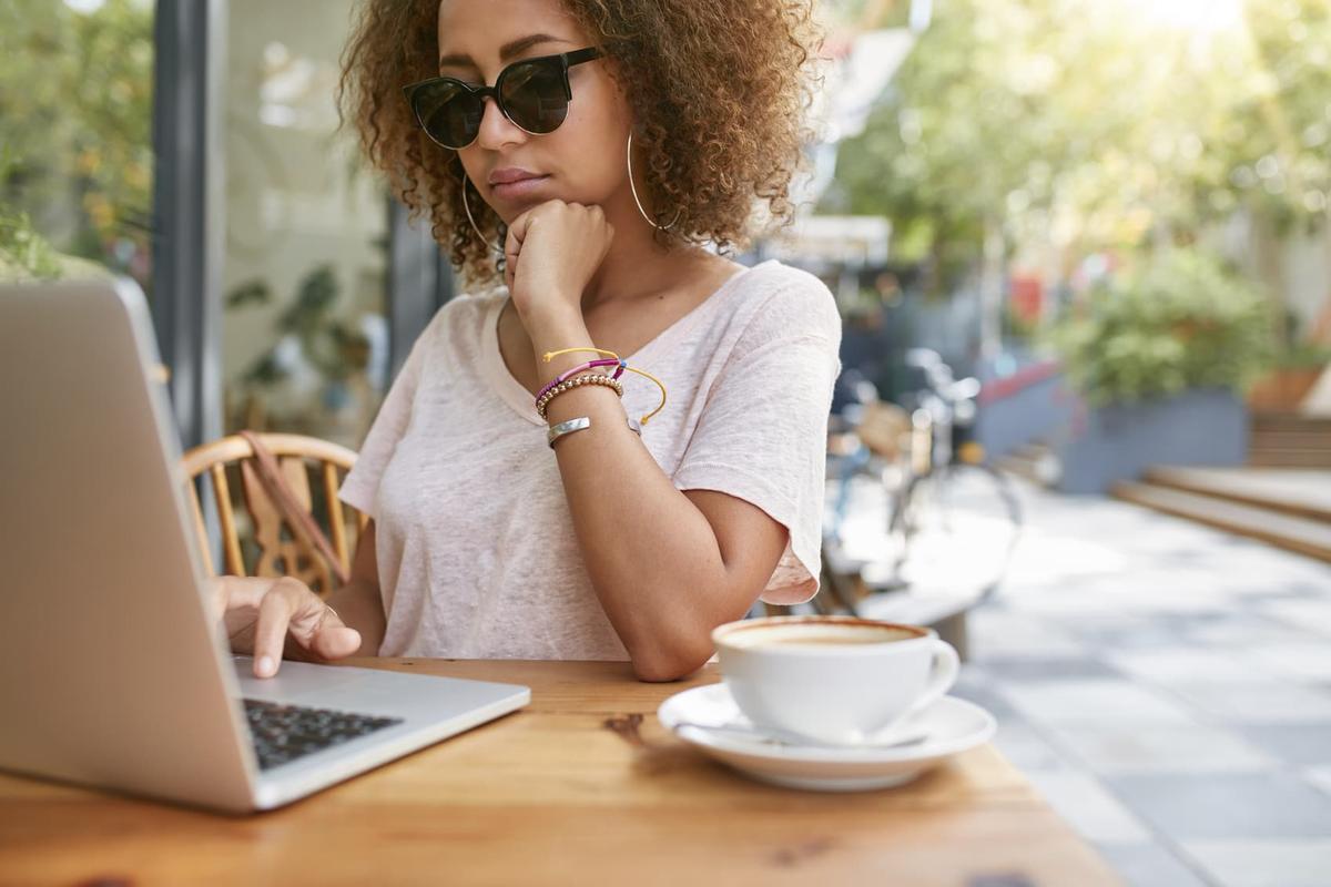 Young woman at outdoor cafe with coffee and laptop, showing active sober lifestyle