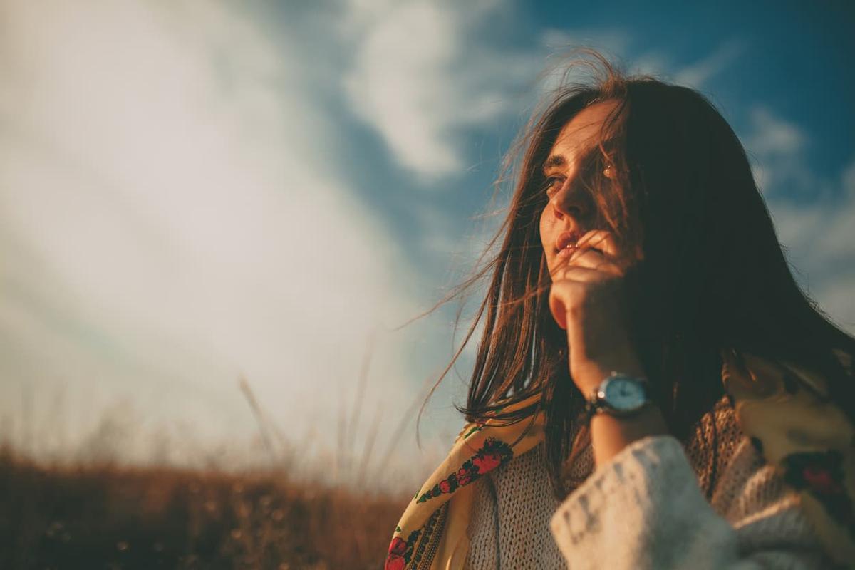 Person standing outdoors in warm, natural light, looking thoughtfully into the distance with wind blowing through her hair, symbolizing reflection, hope, and emotional healing during early recovery.