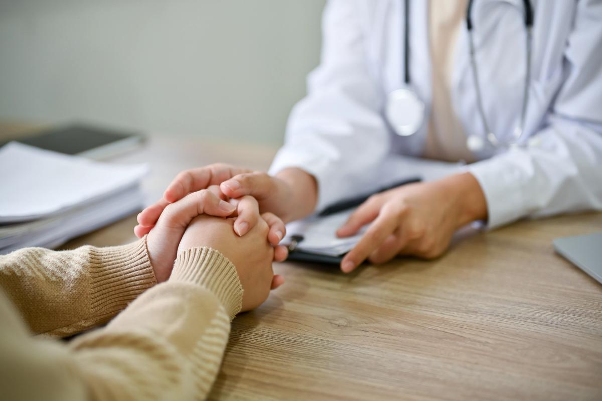 A healthcare provider gently holding a patient’s hands across a desk, symbolizing compassionate guidance and support when navigating health insurance for addiction treatment.
