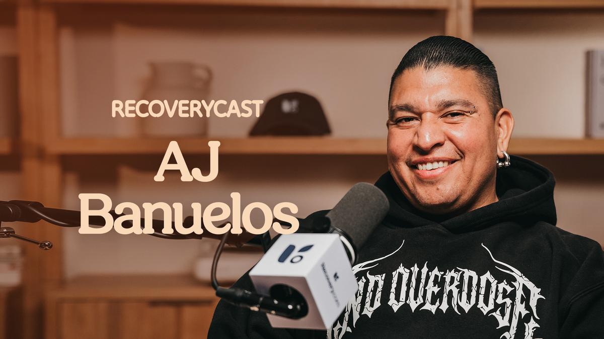 AJ Banuelos wearing a black hoodie that reads "End Overdose" while sitting in front of a microphone recording an episode of Recoverycast.