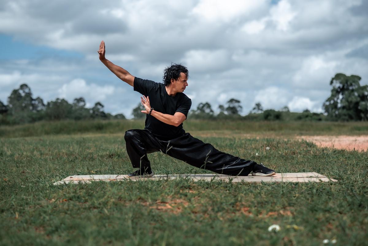 A man wearing all black doing Tai Chi in a lush field.