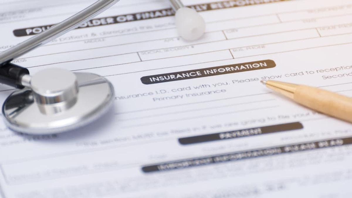 Close-up of a medical insurance information form with a stethoscope and a gold pen resting on it.