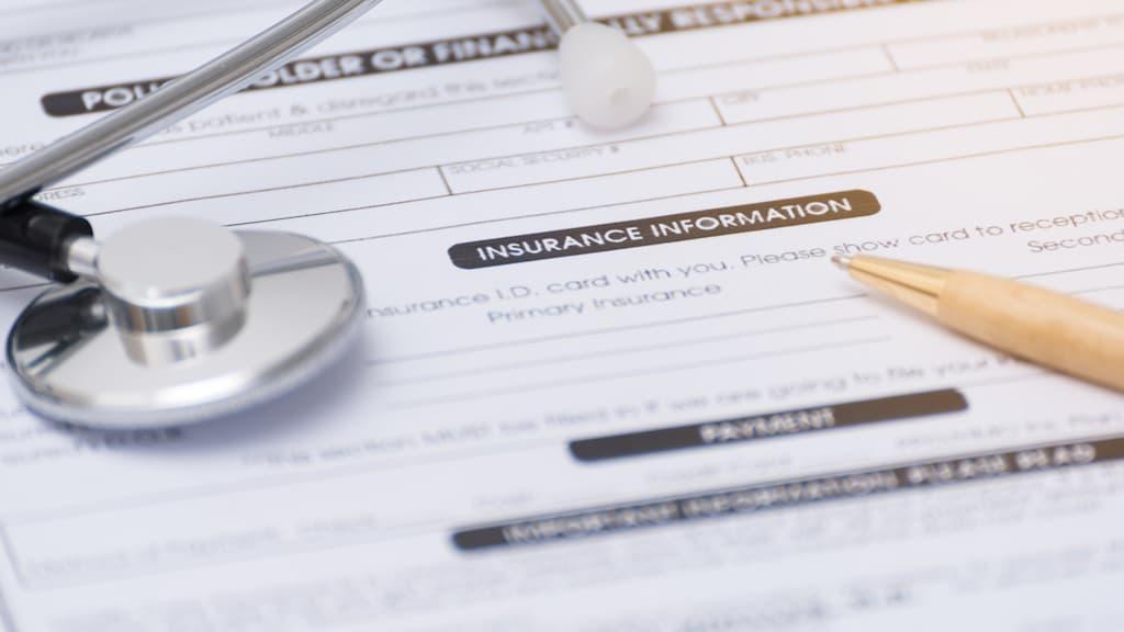 Close-up of a medical insurance information form with a stethoscope and a gold pen resting on it.