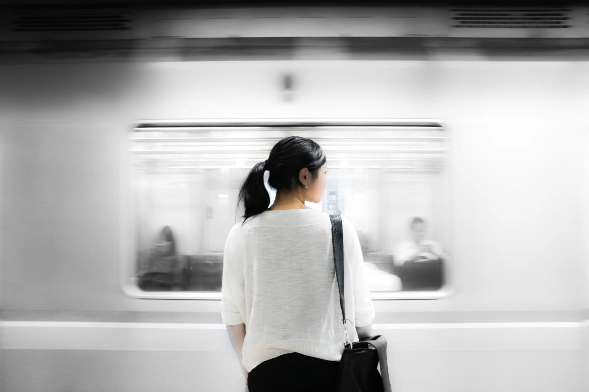 Person standing on a subway platform, seen from behind, as a train rushes past in motion blur, creating a quiet, contemplative moment amid movement.