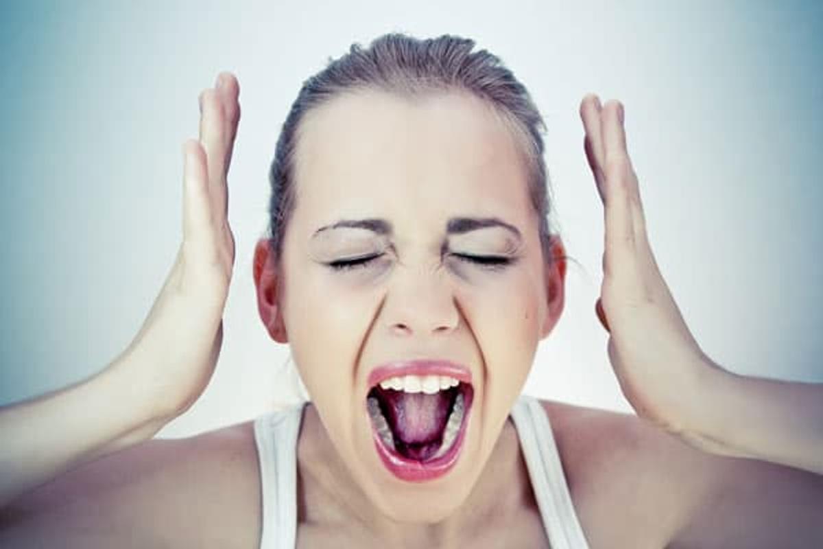 Person screaming with hands raised to head and eyes closed, expressing intense frustration and emotional overwhelm associated with PMS symptoms and mood challenges