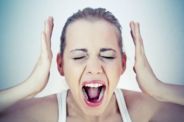 Person screaming with hands raised to head and eyes closed, expressing intense frustration and emotional overwhelm associated with PMS symptoms and mood challenges