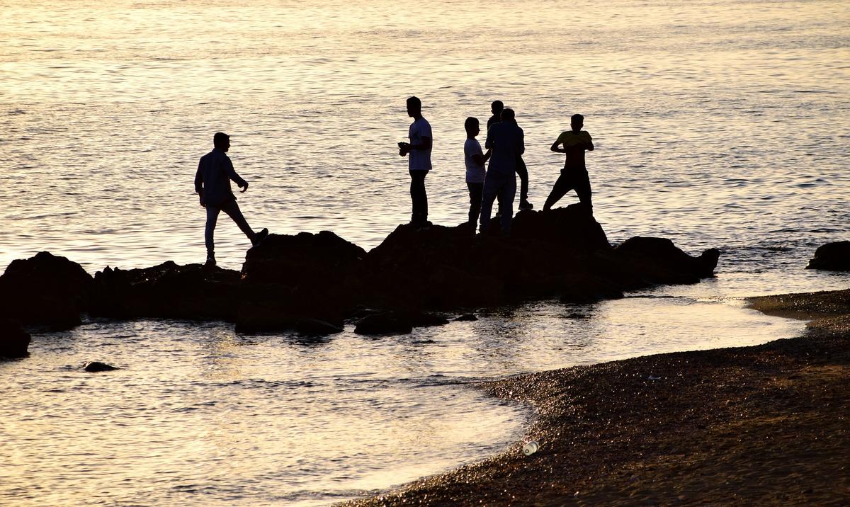 Silhouettes of people standing together on coastal rocks at sunset, representing peer support and community in gender-specific rehab programs