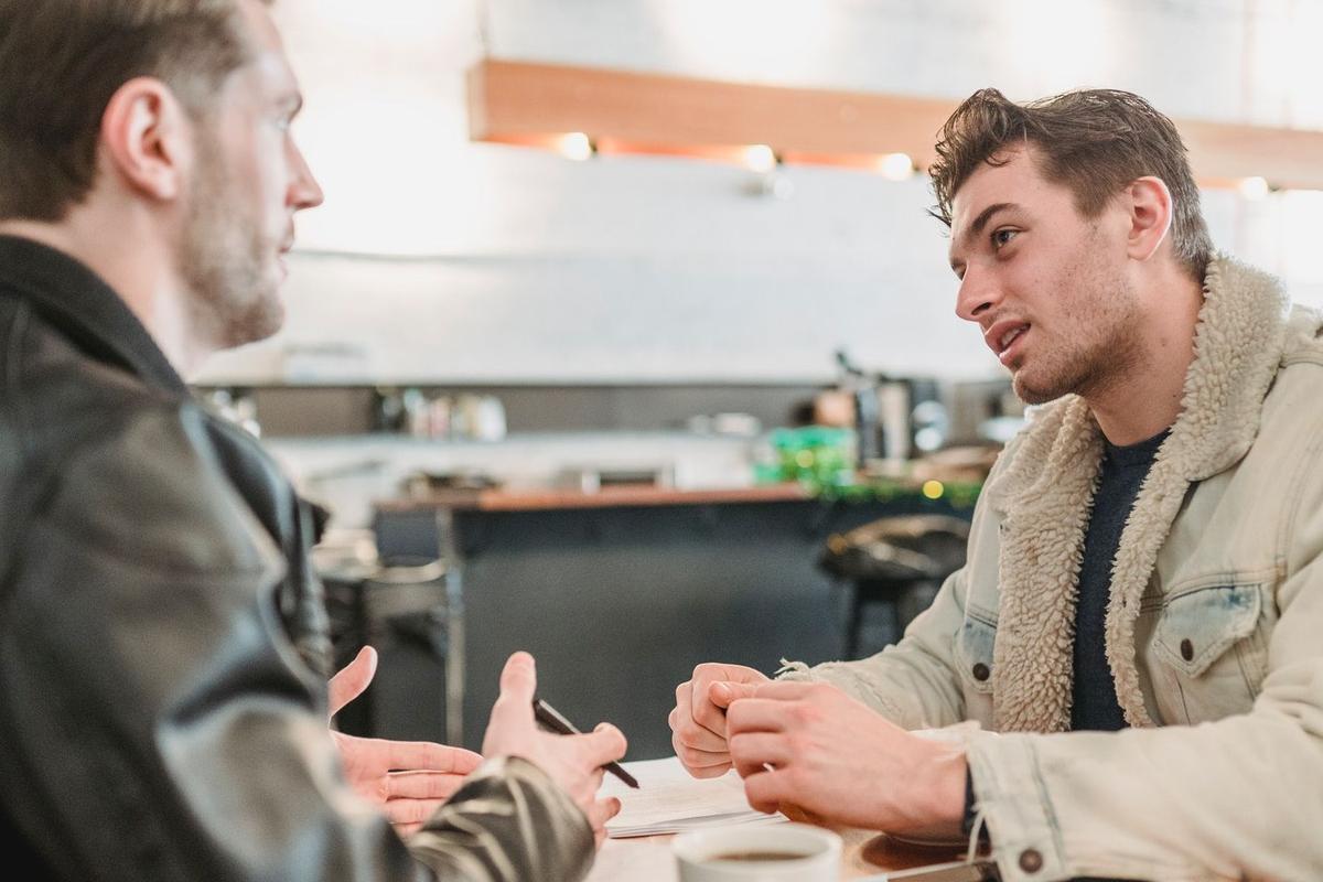 Two men sitting at a table in conversation, representing a sober coach providing guidance and accountability during addiction recovery.