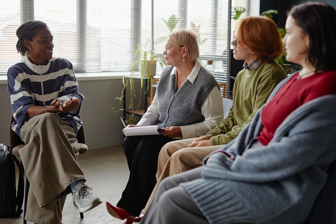 People in a recovery support group talking and connecting during a therapeutic community meeting in a rehab setting.