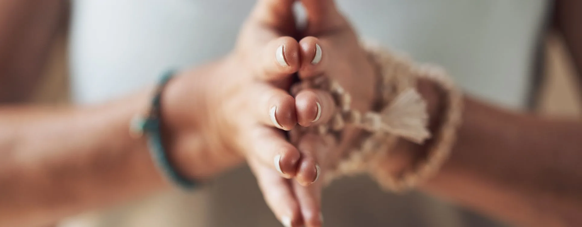 Close-up of hands pressed together in a mindful gesture, wearing natural bracelets, symbolizing spirituality, meditation, and inner peace in recovery.