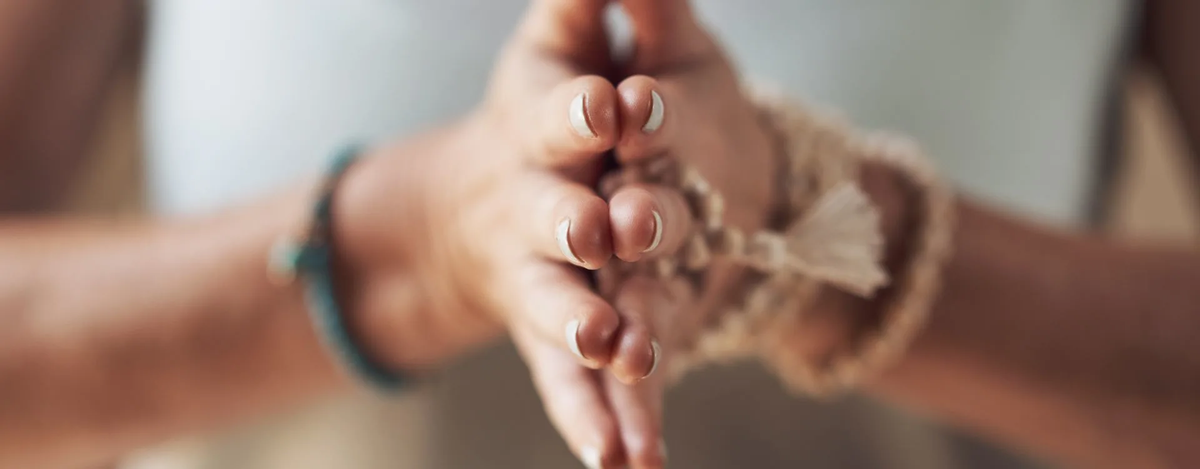Close-up of hands pressed together in a mindful gesture, wearing natural bracelets, symbolizing spirituality, meditation, and inner peace in recovery.
