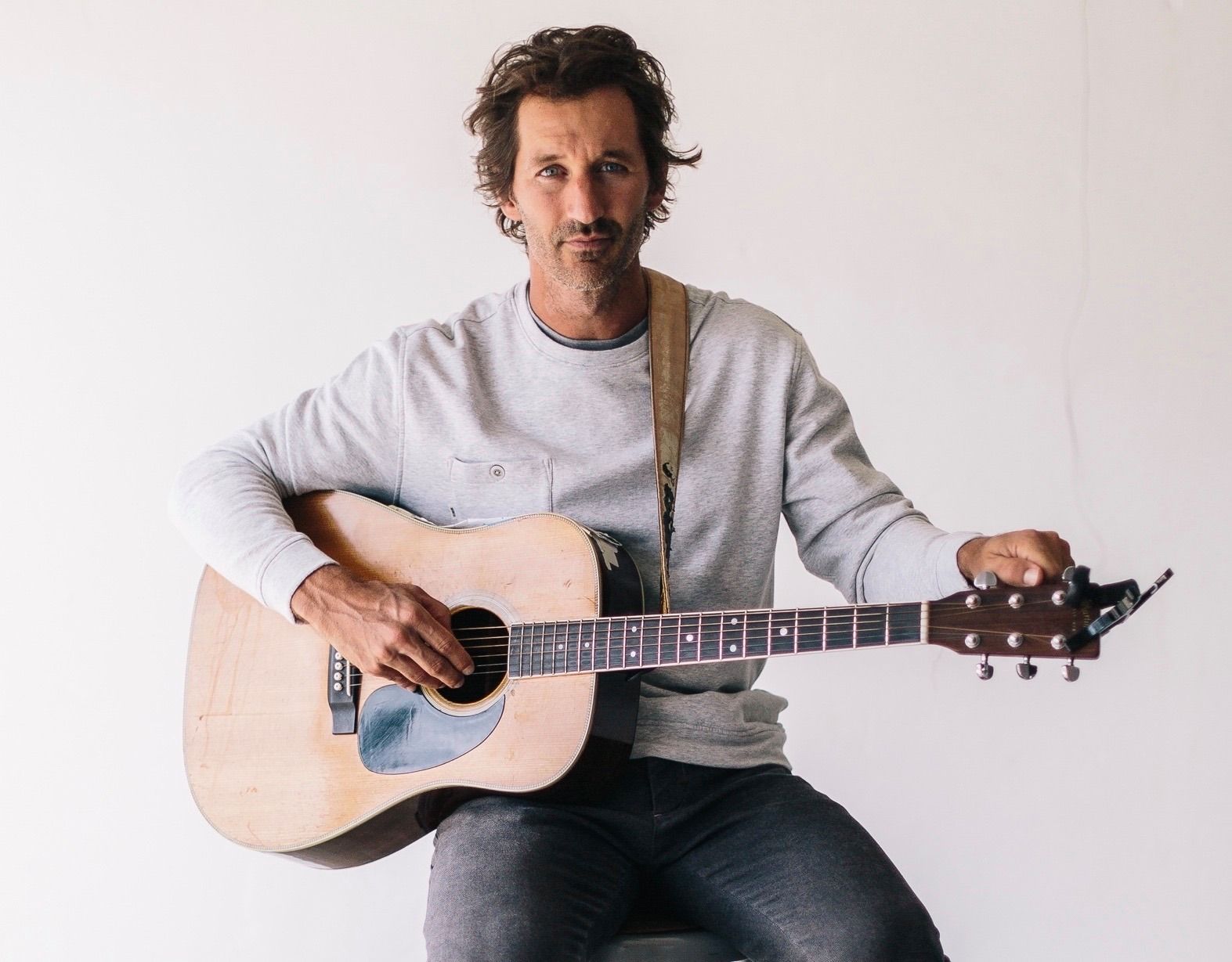 Griffin House holding a guitar while sitting on a stool.