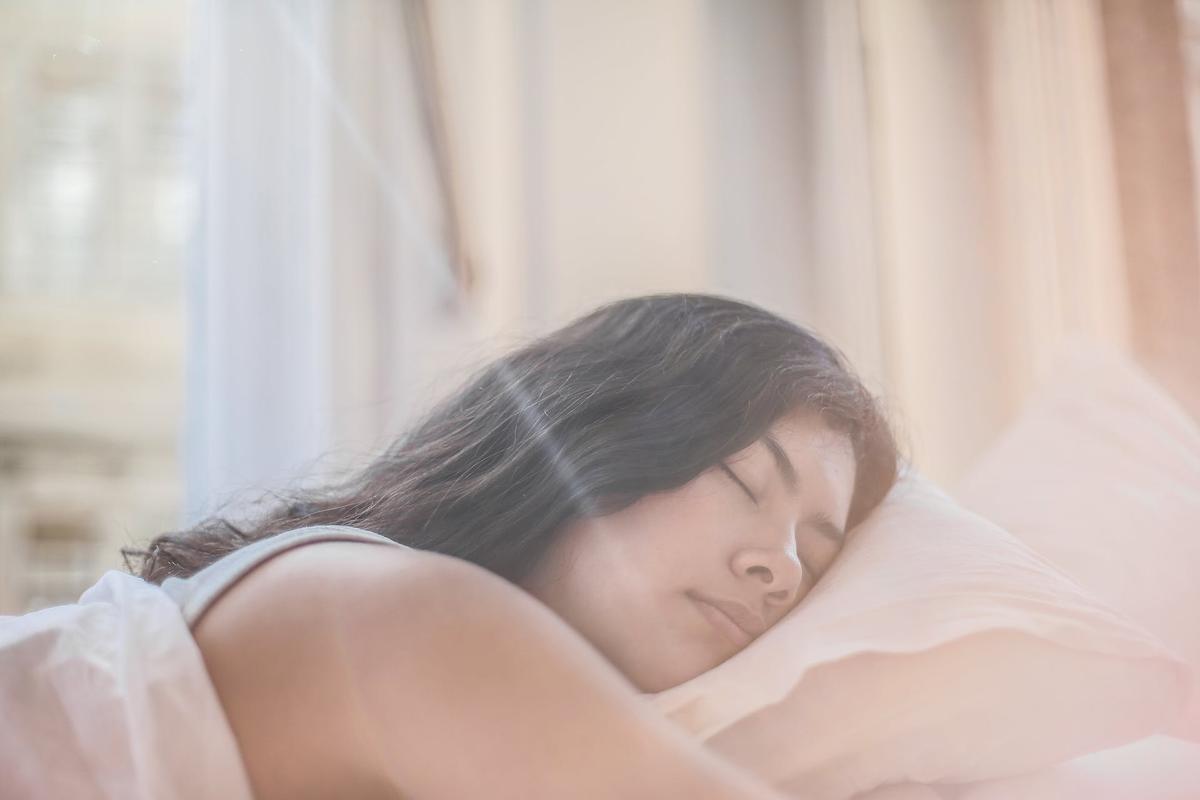 Young woman enjoying restful, quality sleep in serene bedroom setting, showing the connection between sleep and mental well-being