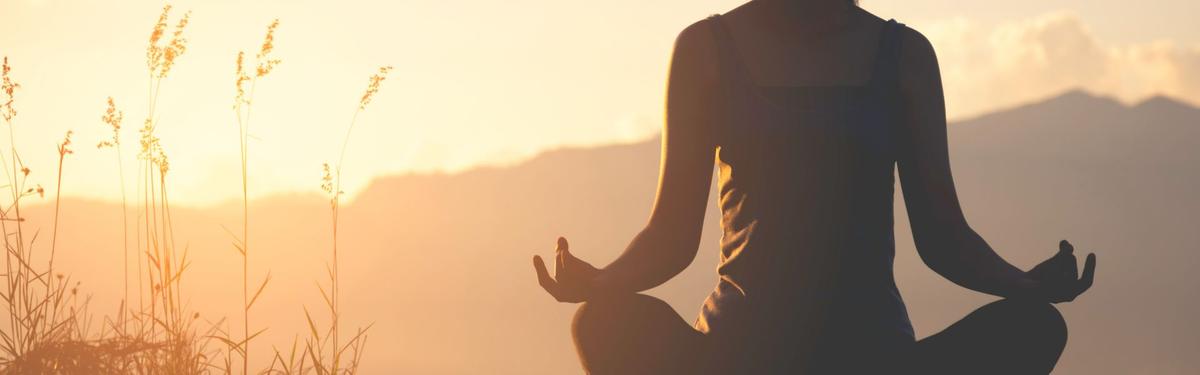 A silhouetted person sitting in a meditative yoga pose outdoors during a golden sunset.