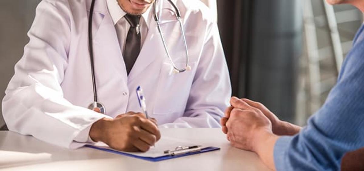 Doctor in a white coat meeting with a patient and taking notes during a consultation, representing support and guidance to quit using cocaine.