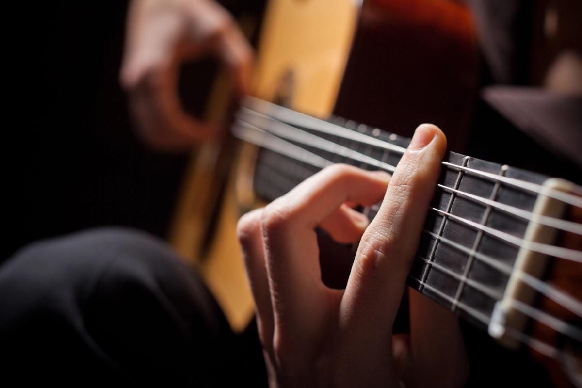A detailed shot focusing on a guitarist's left hand pressing down on the strings of a fretboard to form a chord.