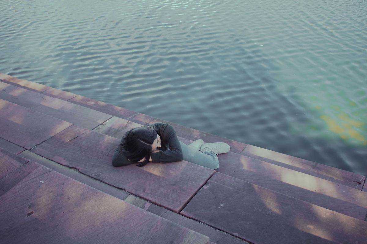 Person sitting alone on steps next to a body of water, representing the isolation that can accompany schizophrenia and the importance of seeking treatment and support