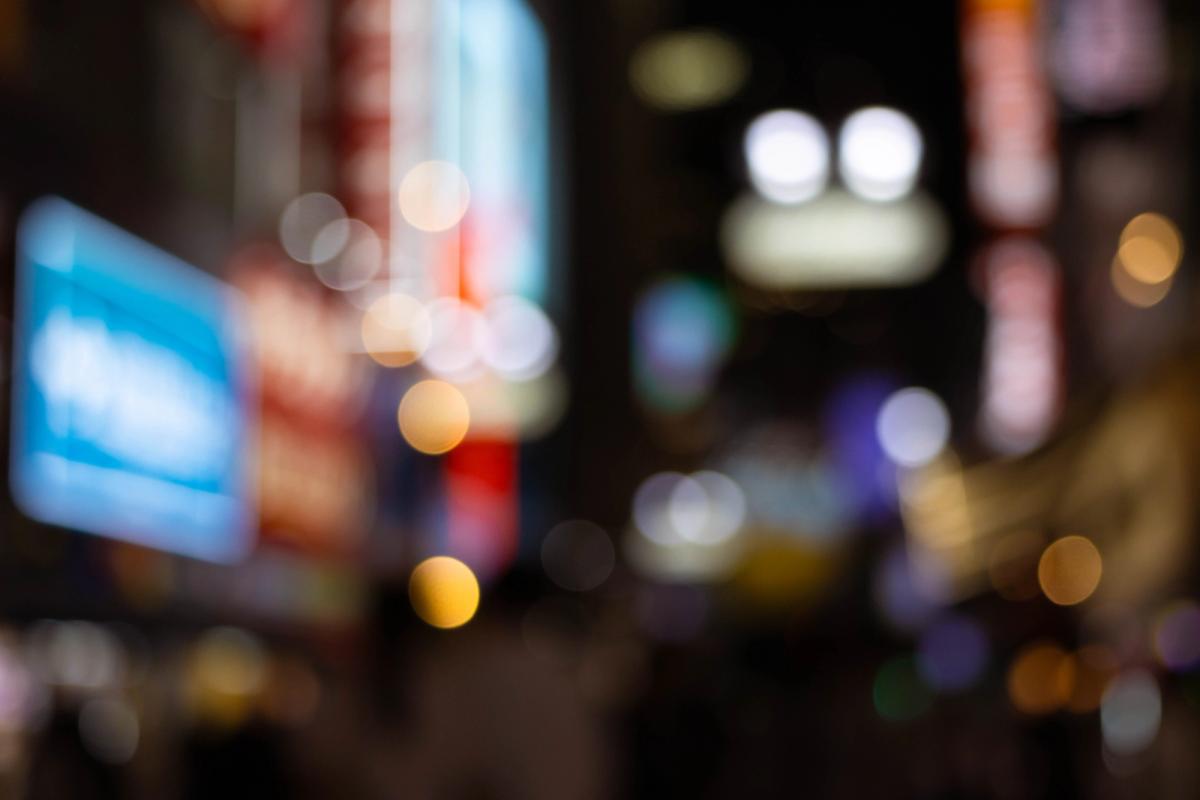 Blurred city street at night with out-of-focus lights and illuminated signs creating a bokeh effect.