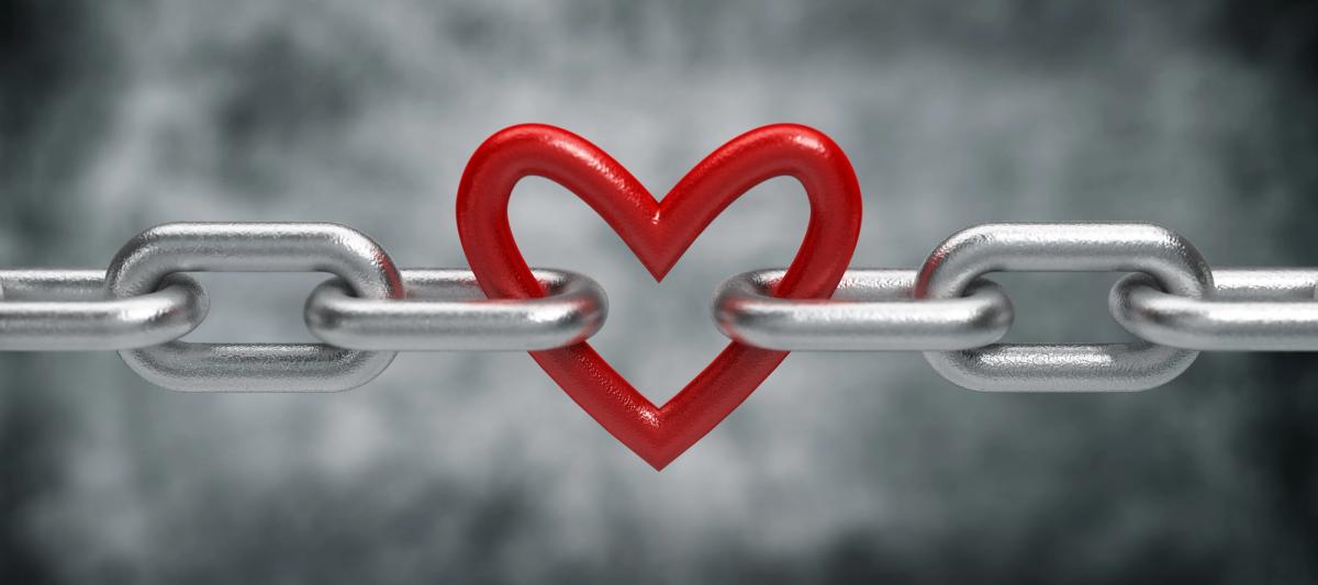 A horizontal silver metal chain with a vibrant red, heart-shaped link in the center, connecting two segments against a blurred gray background.