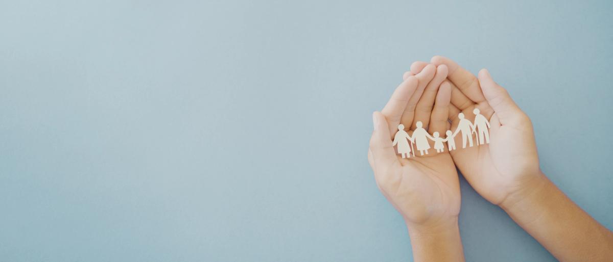 Two hands cupped together holding a white paper cutout chain of a multi-generational family against a light blue background.